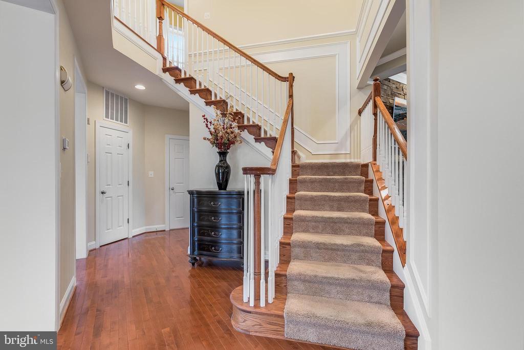 Foyer with a carpeted staircase, wood railings, hardwood floors, and a dark chest with flowers.
