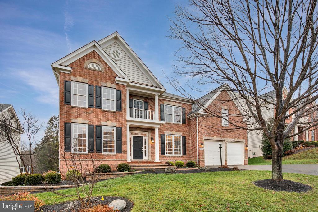Two-story brick home with black shutters, a small balcony, and an attached two-car garage.