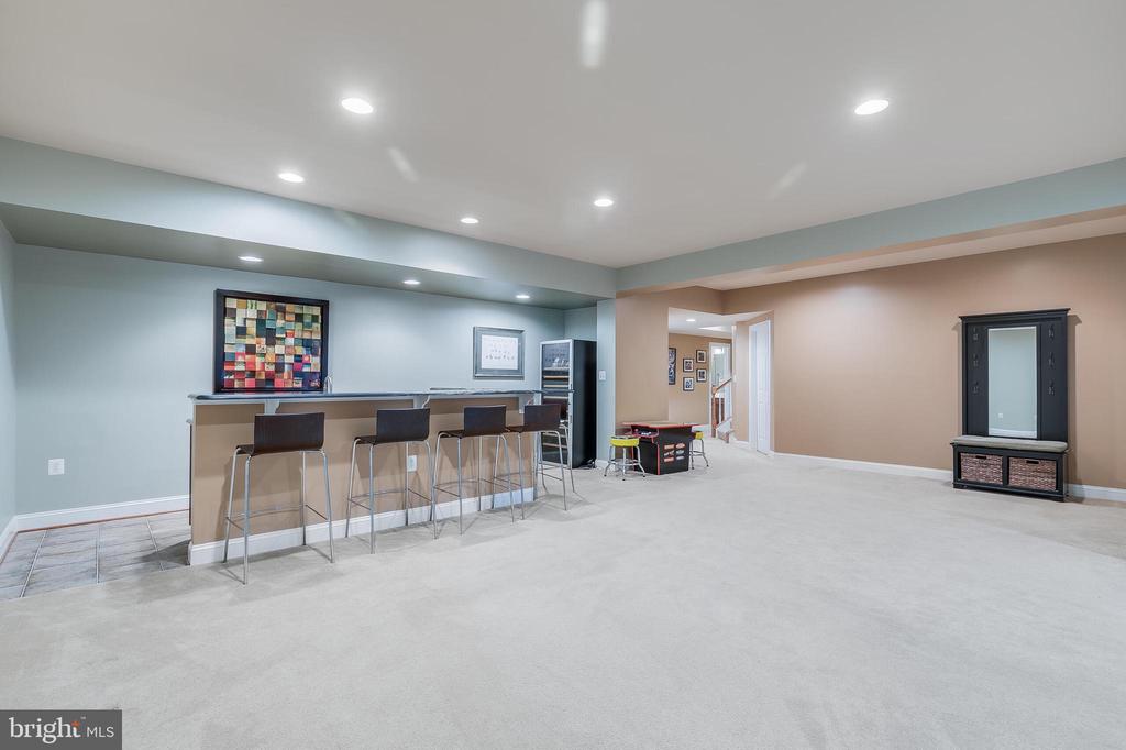 Finished basement recreation room with a bar, stools, and game table.