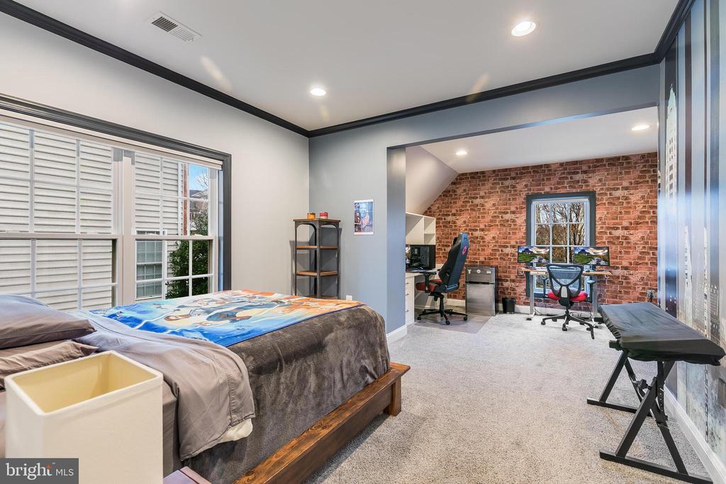 Bedroom with large windows and an adjoining office featuring an exposed brick wall.