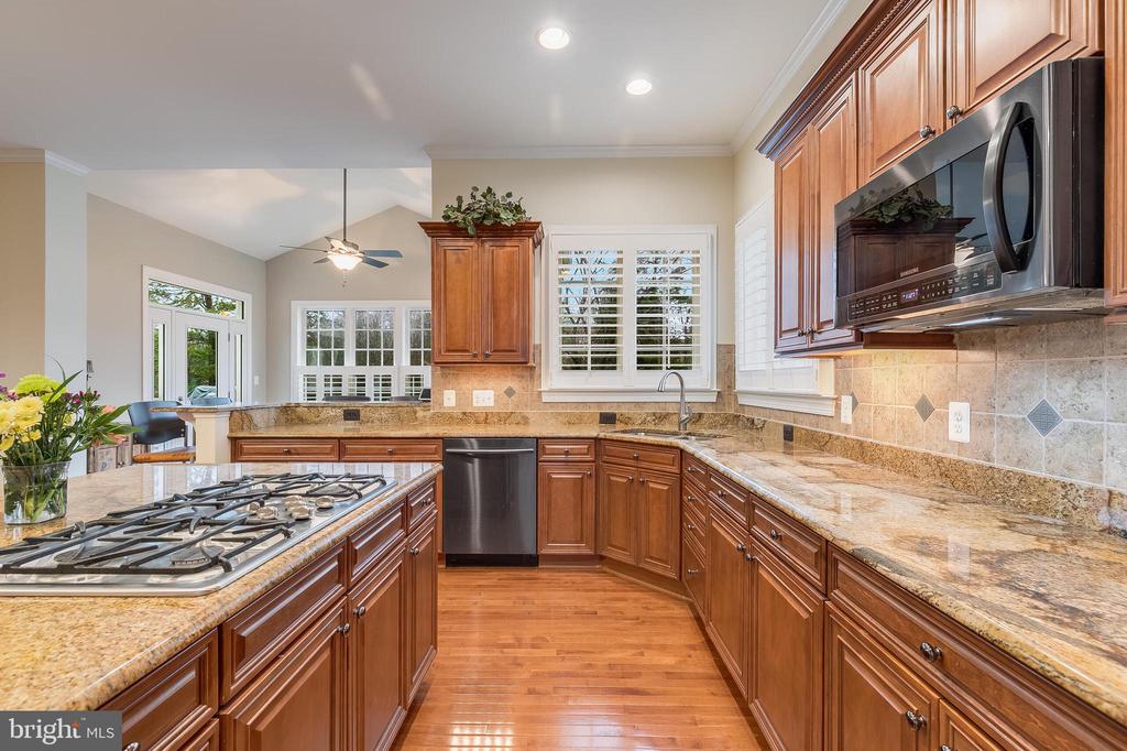 Kitchen with rich wood cabinets, granite countertops, a cooktop island, and hardwood floors.