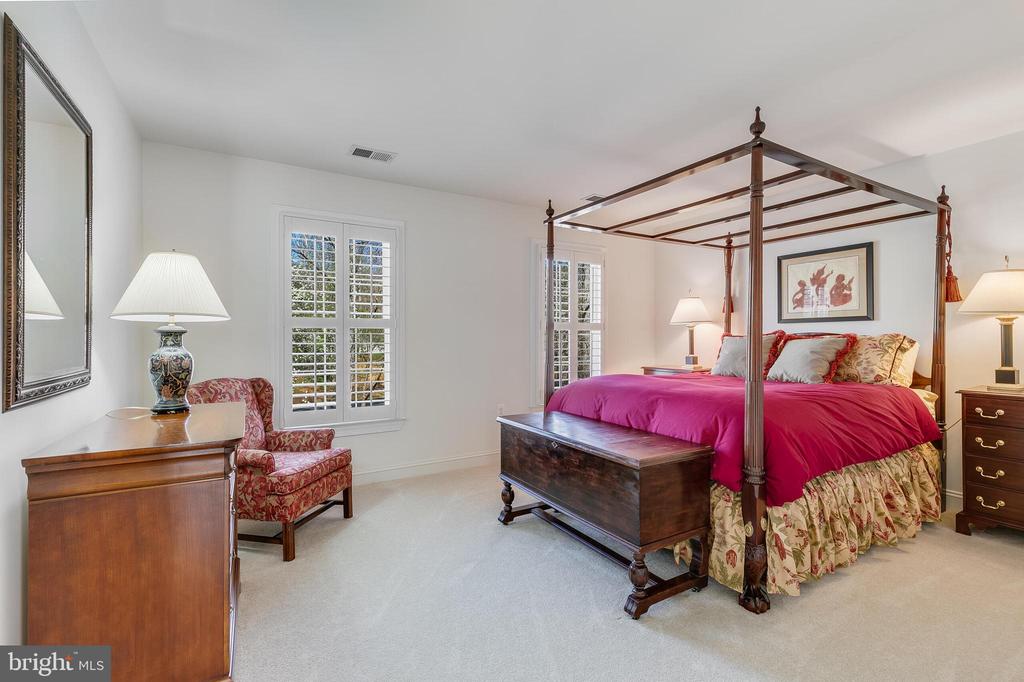 Bedroom with a four-poster bed, magenta bedding, floral furnishings, and shuttered windows.