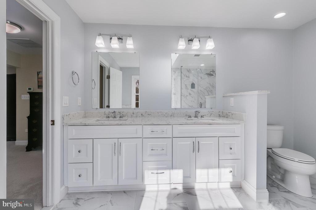 Primary bathroom with a long double vanity, marble-patterned counters, and a separate toilet nook.