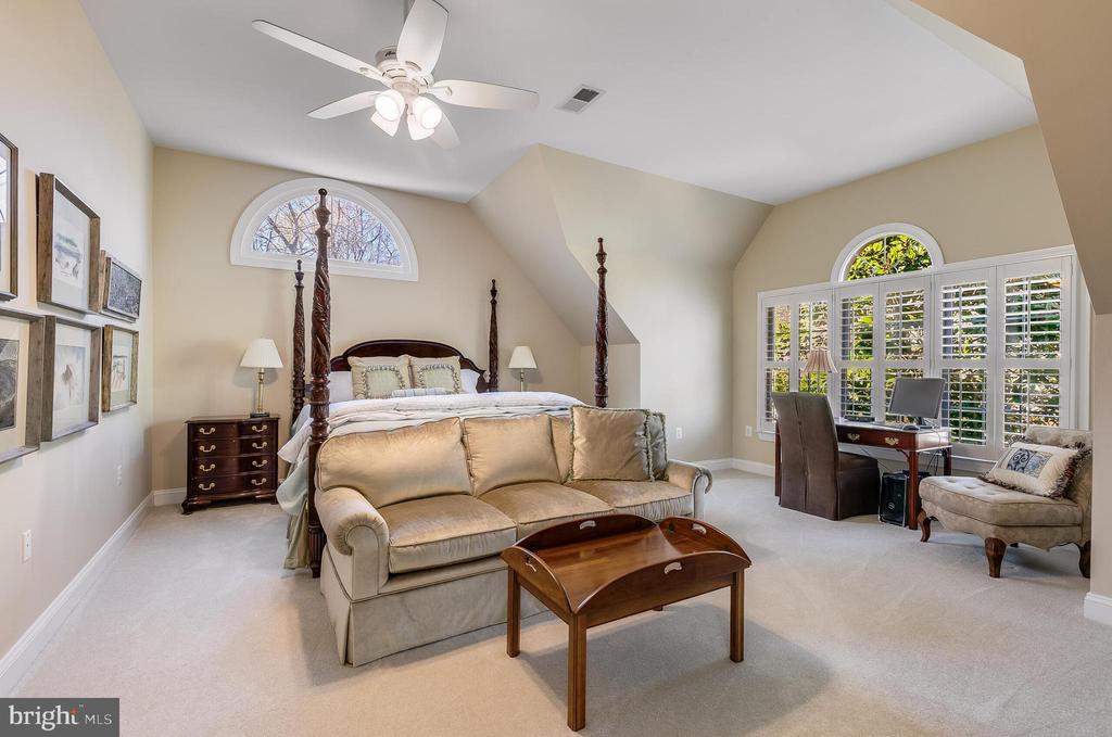 Furnished bedroom with a four-poster bed, beige sofa, and desk beside plantation-shuttered windows.