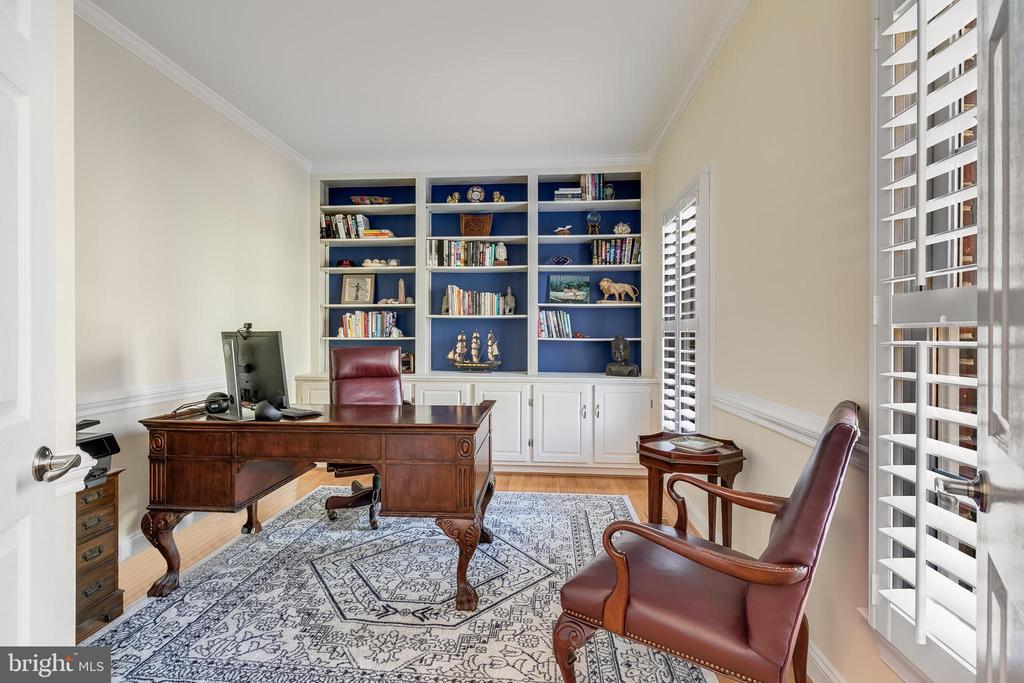 Home office with built-in blue-backed bookshelves, a dark wood desk, and leather chairs.