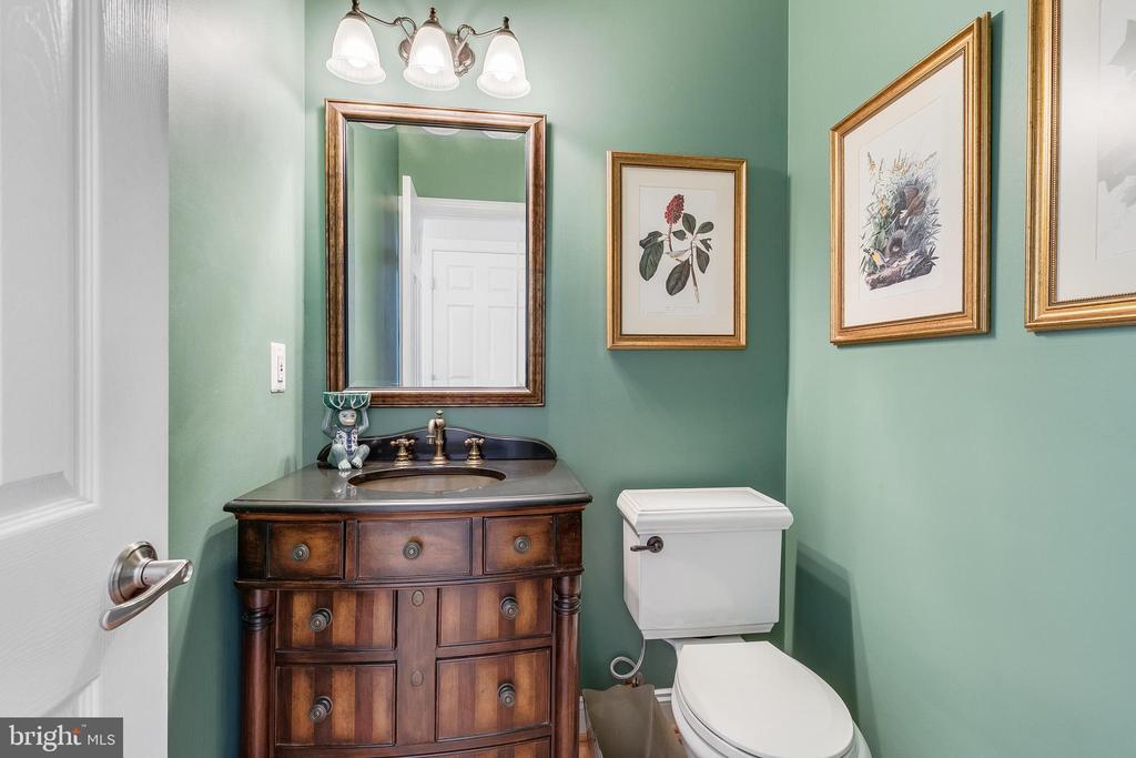 Powder room with a dark wood vanity, white toilet, sage green walls, and framed botanical artwork.