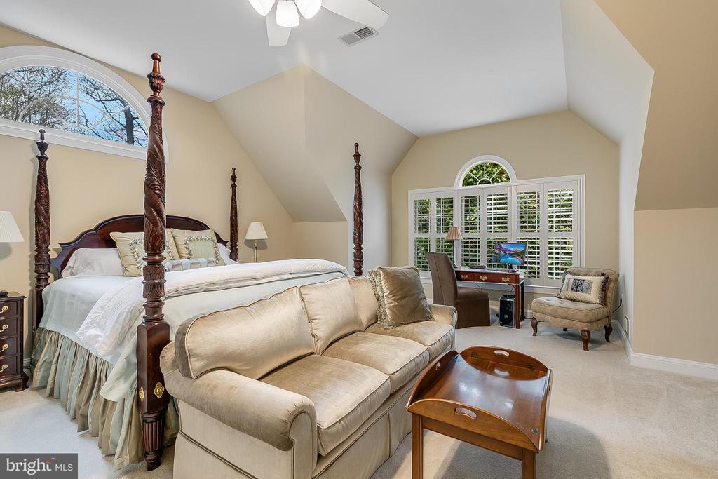 Furnished bedroom with a four-poster bed, beige sofa, and desk by shuttered windows.