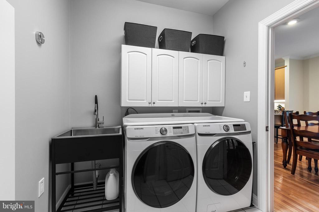 Laundry room with front-loading washer and dryer, deep utility sink, and overhead storage cabinets.