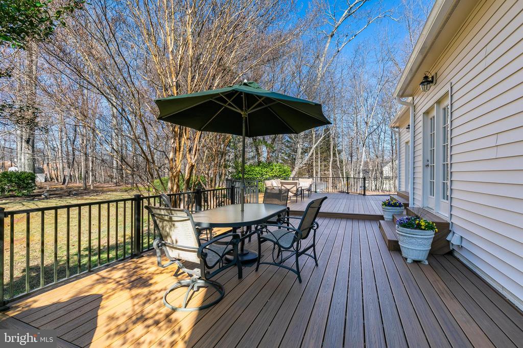 Spacious deck with patio dining sets and umbrella overlooking a wooded backyard.