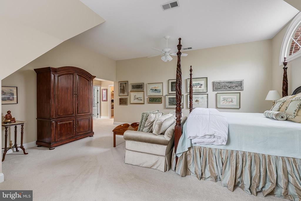 Bedroom with a four-poster bed, upholstered settee, and dark wood armoire.