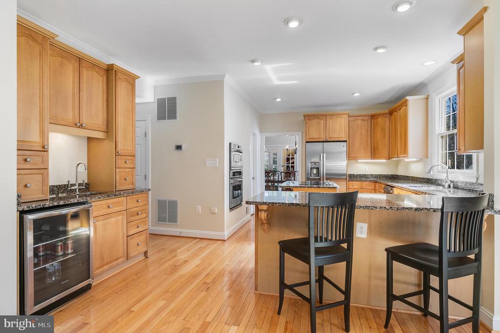 Kitchen with a large granite island, honey-colored cabinets, hardwood floors, and stainless steel appliances.