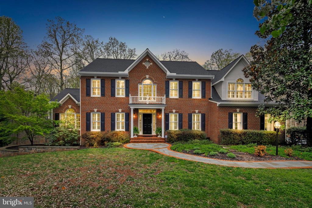 Two-story brick home with illuminated windows, dark shutters, and a curved front walkway.