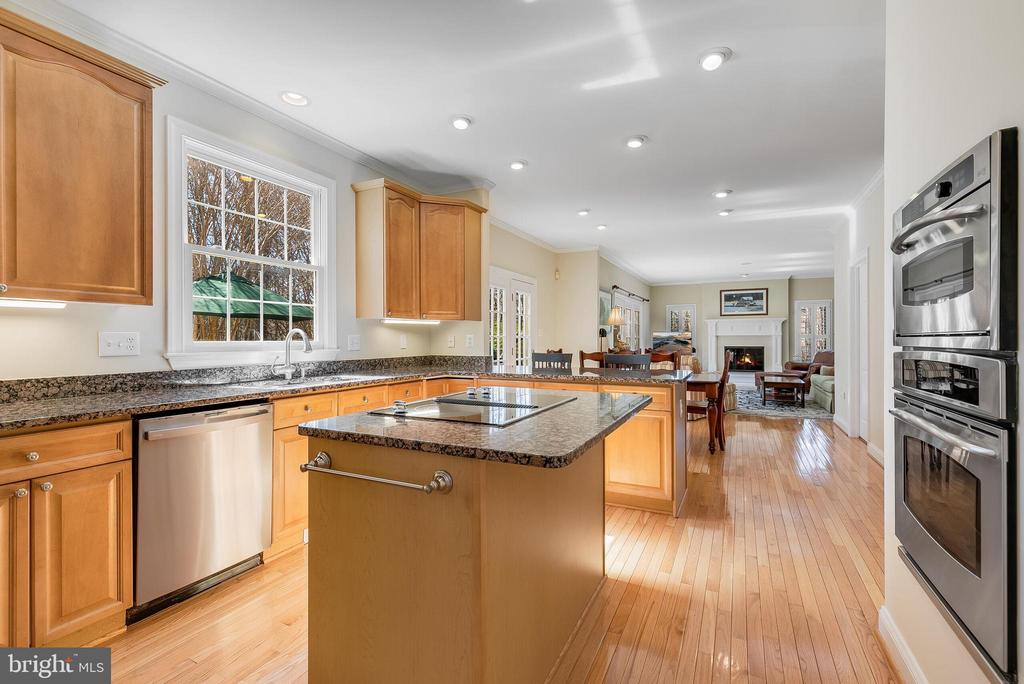 Kitchen with granite island, wood cabinetry, stainless appliances, and an adjoining living room.