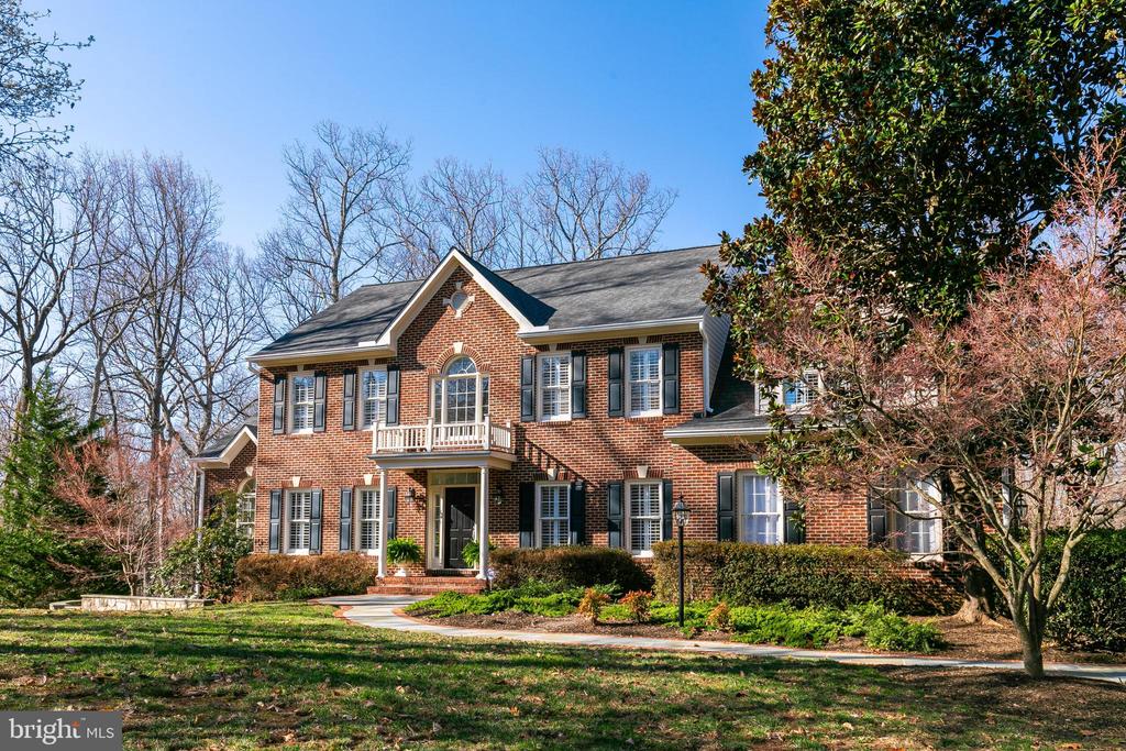Two-story red brick house with black shutters, a small balcony, and landscaped front grounds.