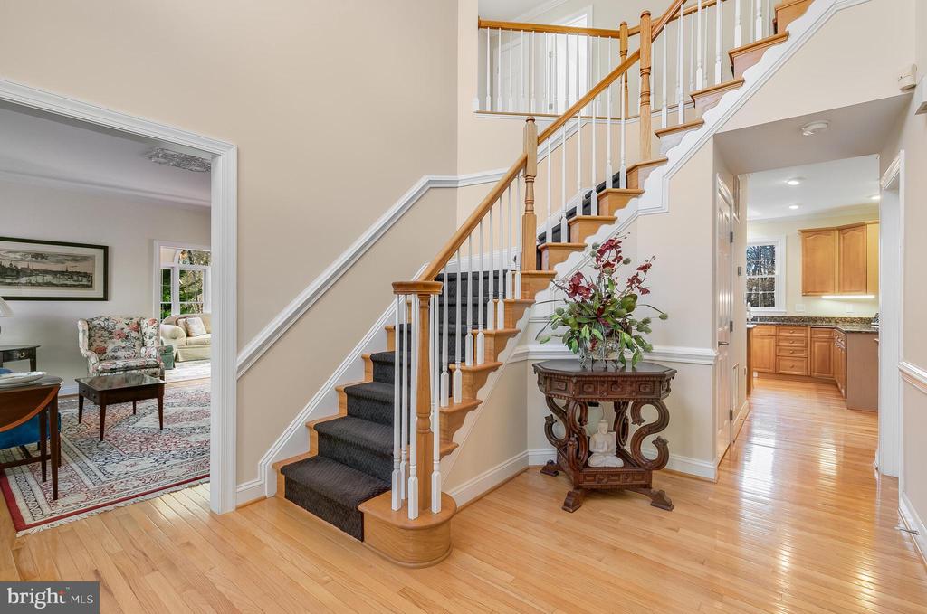 Foyer with a curved staircase, hardwood floors, and views into a sitting room and kitchen.