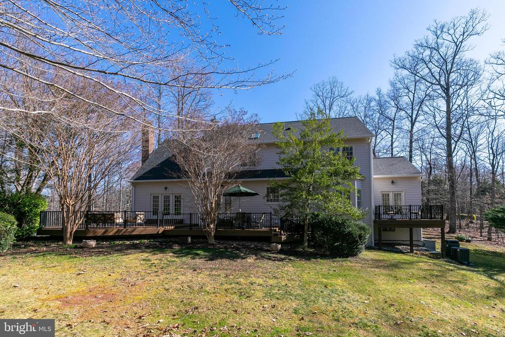 Rear of a two-story gray house with a wide deck and wooded yard.