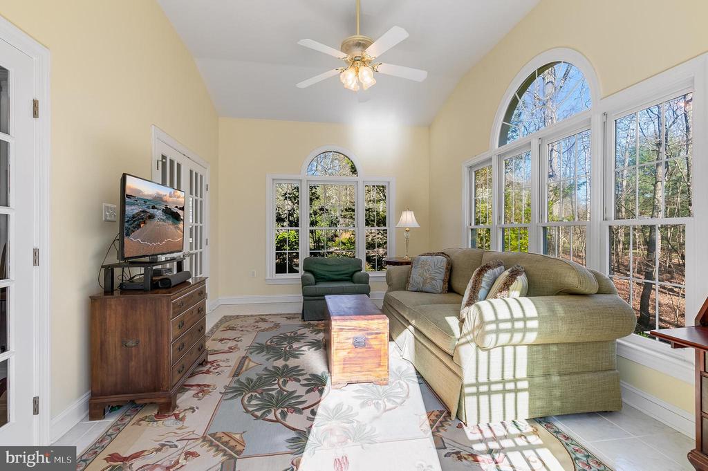 Furnished living room with vaulted ceiling and large arched windows overlooking trees.