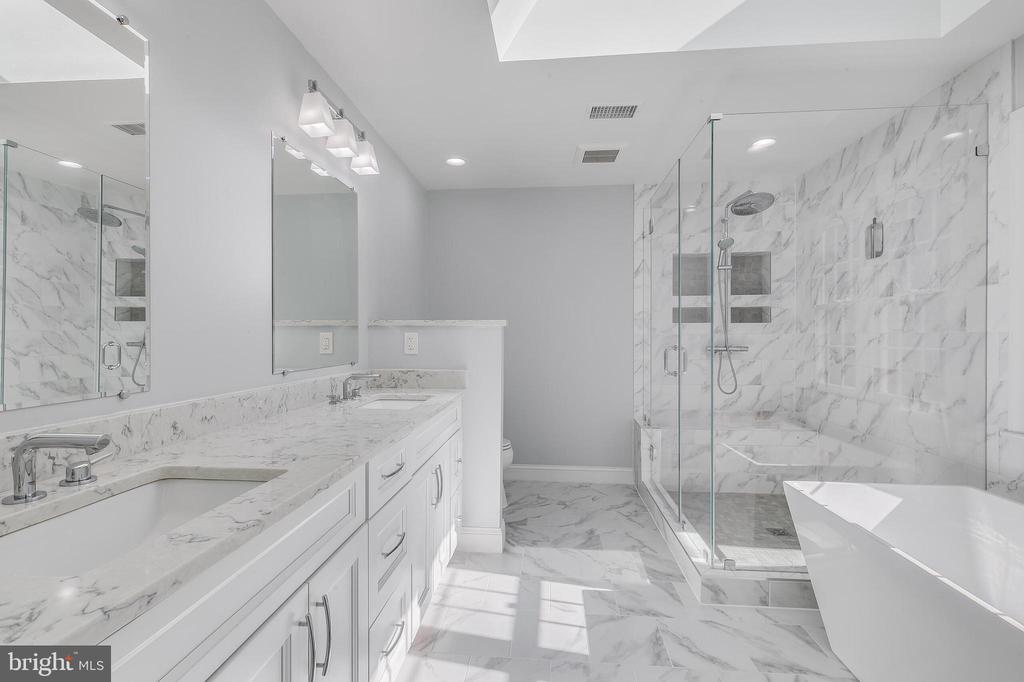 Primary bathroom with a marble double vanity, glass shower, and freestanding soaking tub.