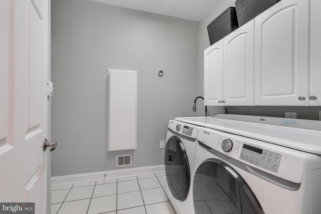 Laundry room with front-loading washer and dryer beneath white cabinets.
