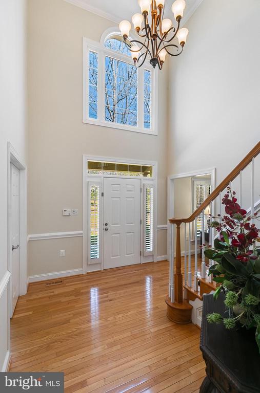 Two-story foyer with hardwood floors, a tall arched window, chandelier, and curved staircase.