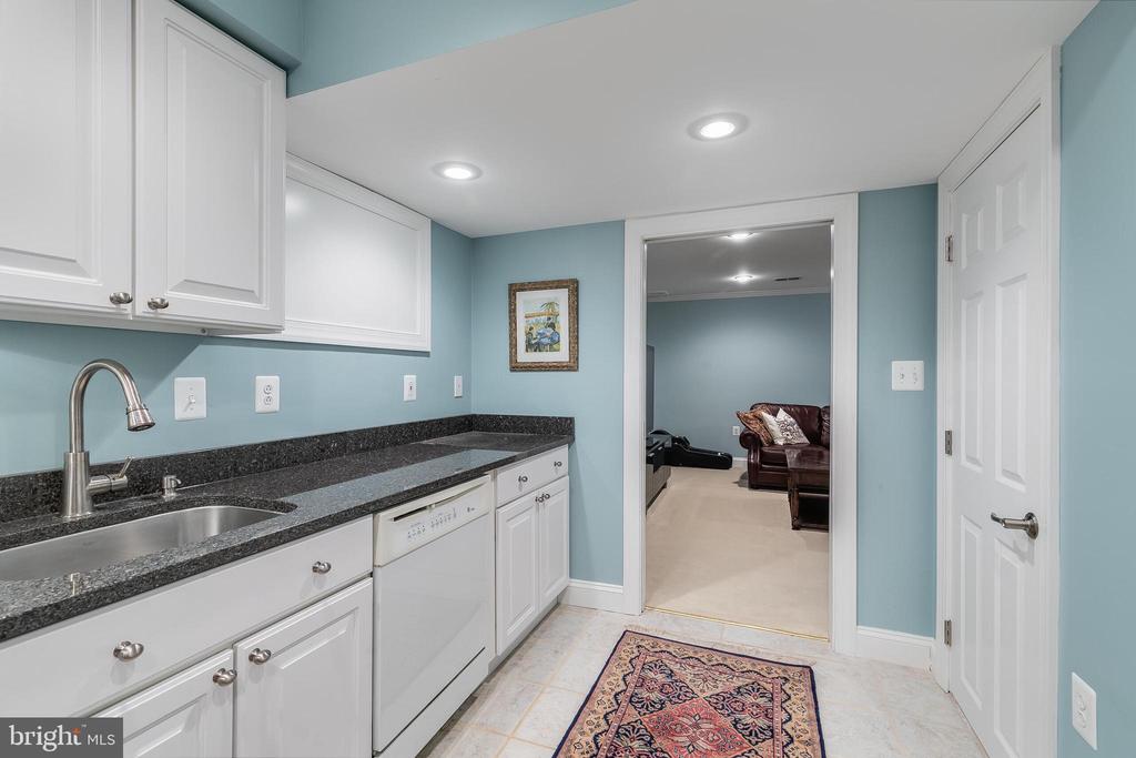 Laundry room with white cabinets, a stainless-steel sink, dark countertops, and a dishwasher.