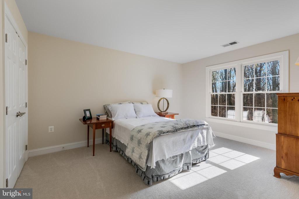 Bedroom with a neatly made bed beside a large window overlooking trees.