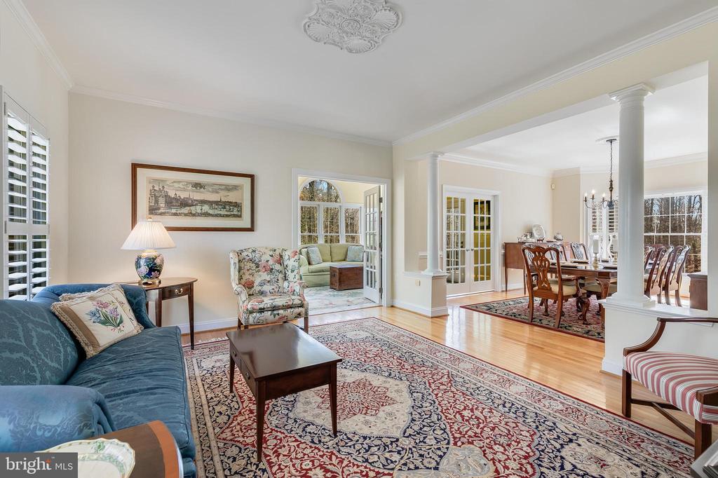 Furnished living room opening to a formal dining room, with hardwood floors and a wide columned opening.