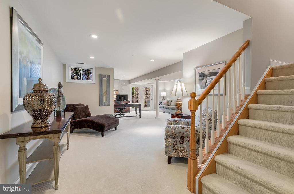 Furnished living area with a carpeted staircase, wood handrail, seating, and a desk.