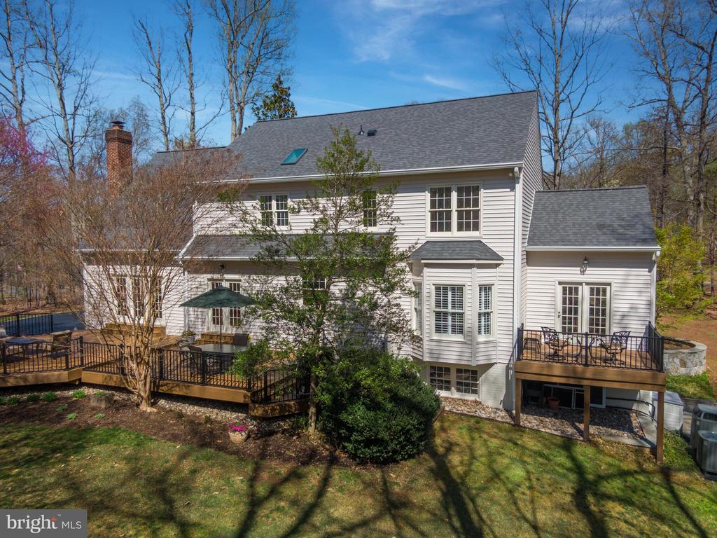 Rear of a white two-story house with multiple decks and a wooded yard.