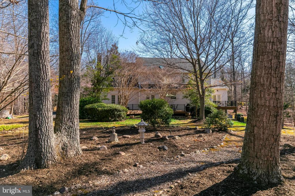 House rear and raised deck framed by mature trees in a landscaped yard.