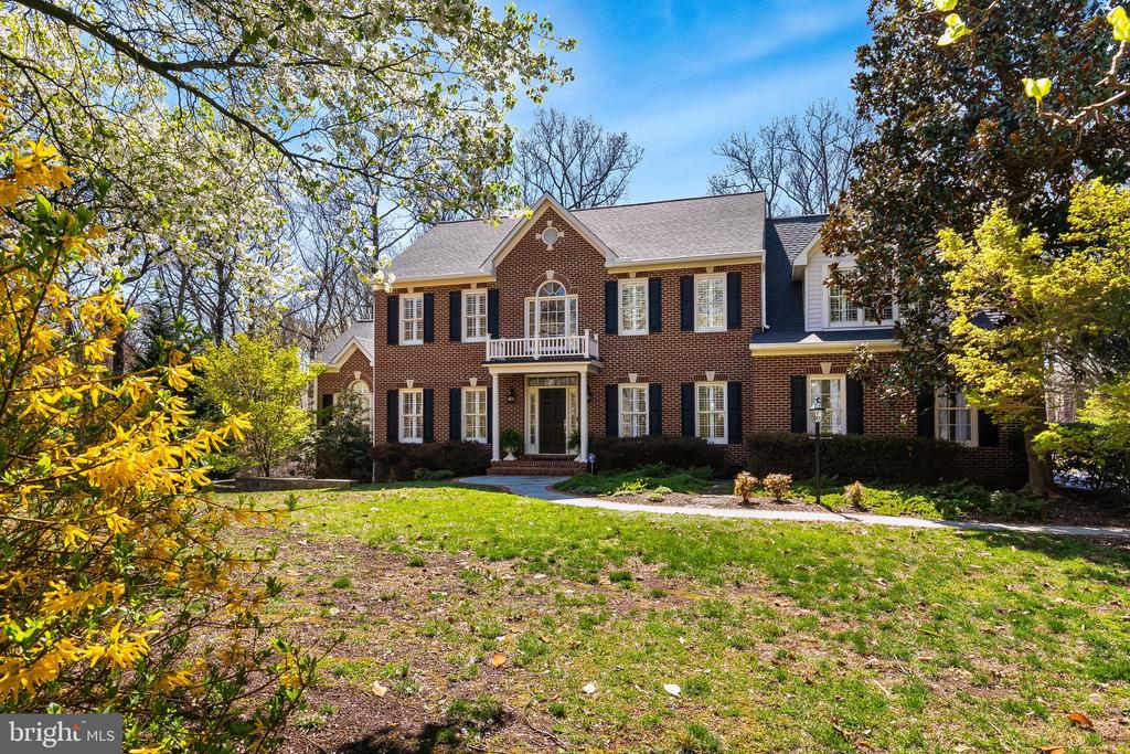 Two-story brick house with a small balcony, white trim, and a tree-framed front lawn.