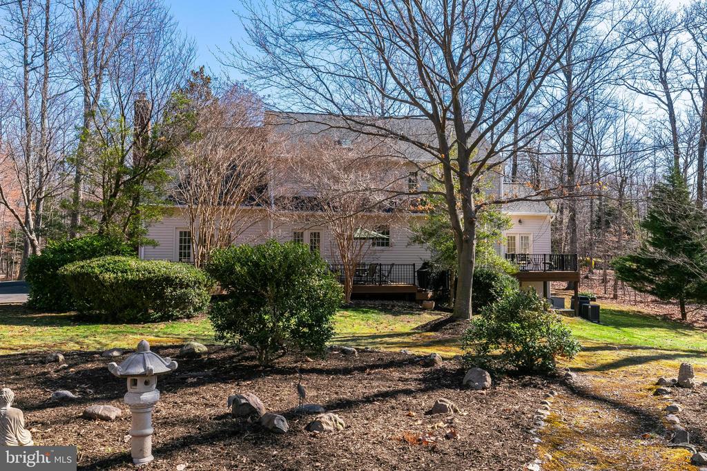 Rear exterior of a two-story home with raised decks, landscaped yard, and leafless trees.
