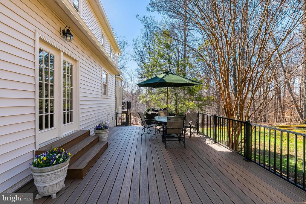 Wooden deck with outdoor dining set and green umbrella overlooking a wooded yard.