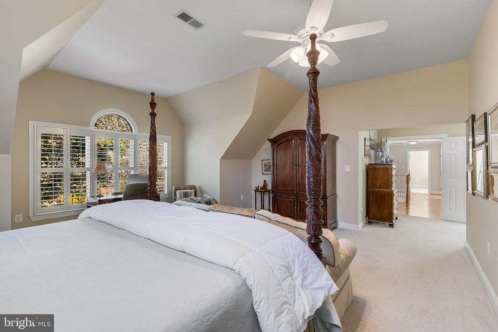 Bedroom with a four-poster bed, vaulted ceiling, plantation shutters, and dark wood armoire.