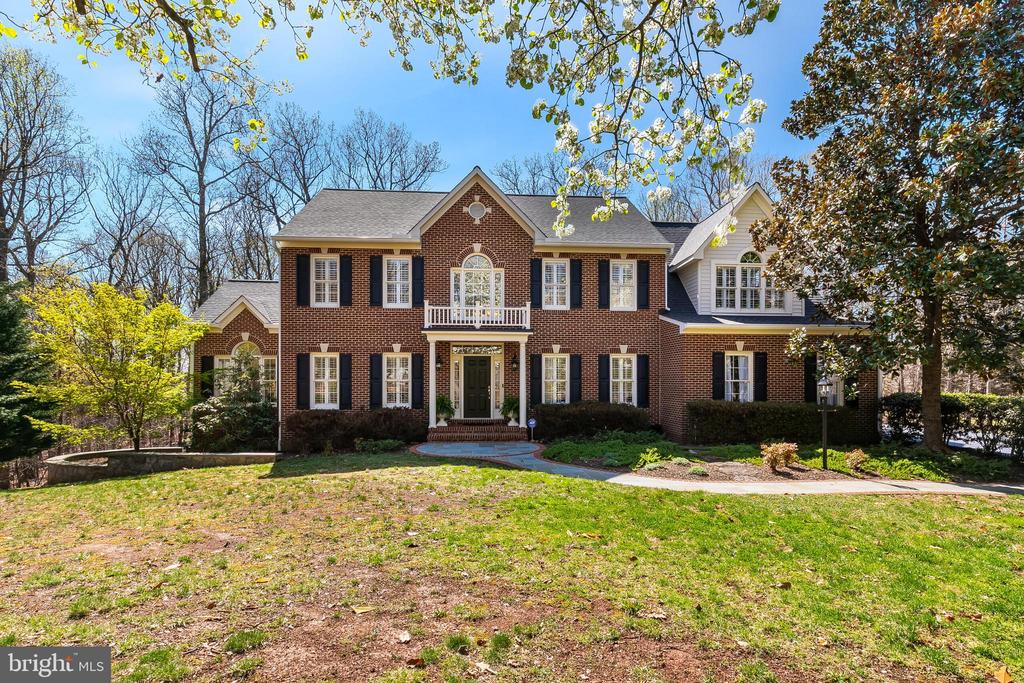 Two-story red-brick home with black shutters, white trim, and a landscaped front lawn.
