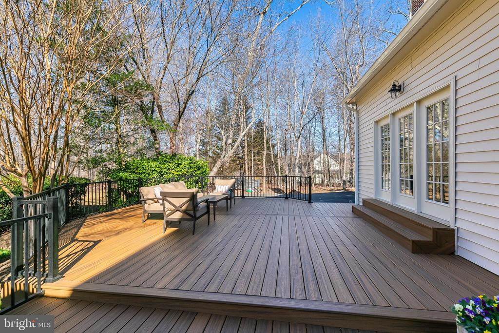 Spacious composite deck with outdoor seating, black railings, and a wooded yard beyond.