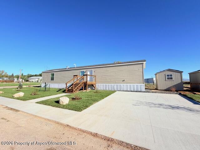 Manufactured home with wooden entry stairs, a broad concrete driveway, and a detached shed.