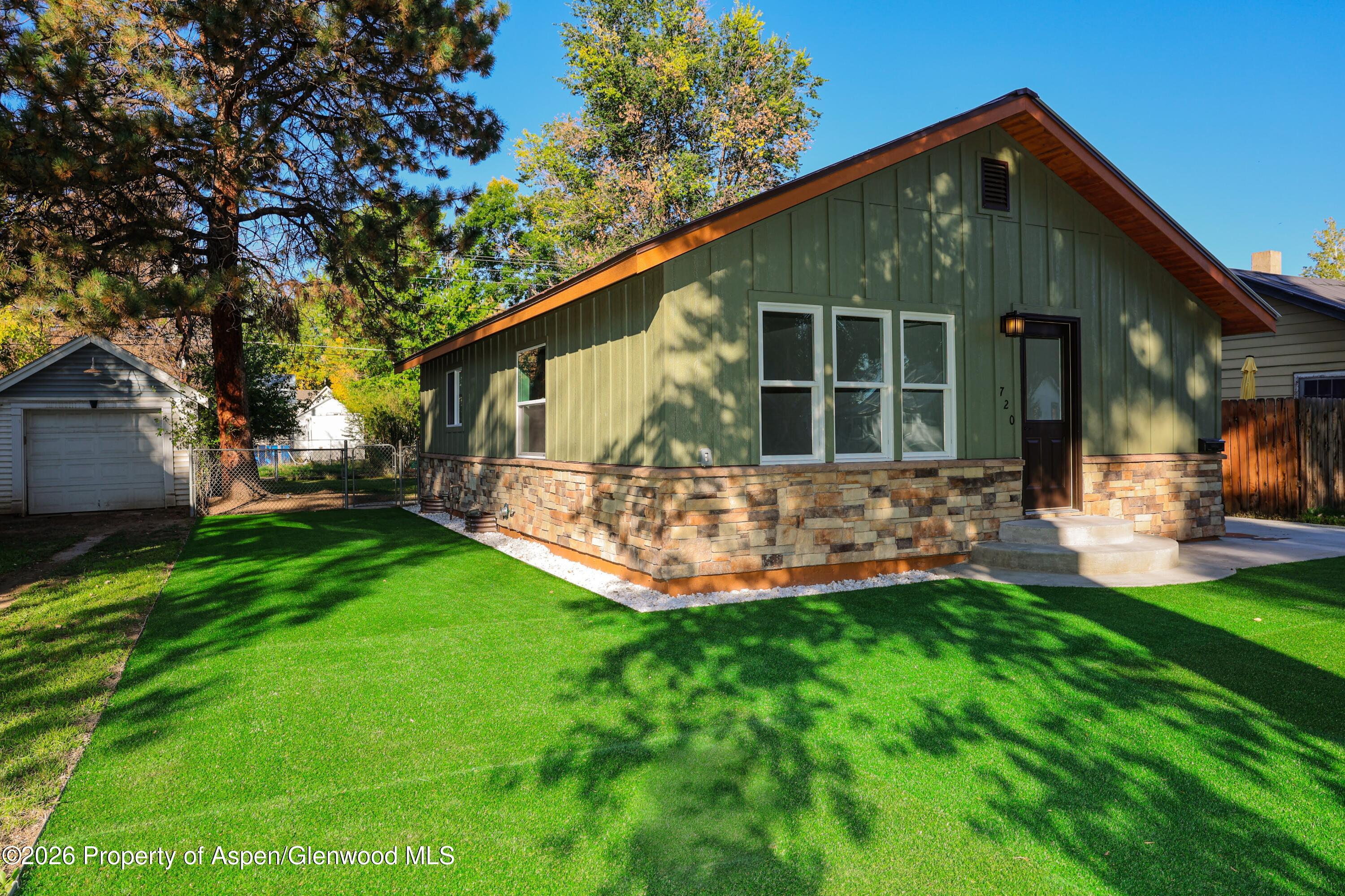 Green-sided home with stone foundation and shaded lawn; detached garage visible beside it.