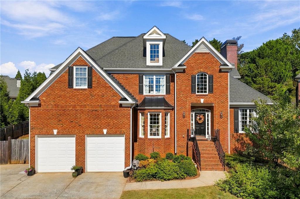 Red brick two-story house with a gray gabled roof, double garage, and brick front steps.