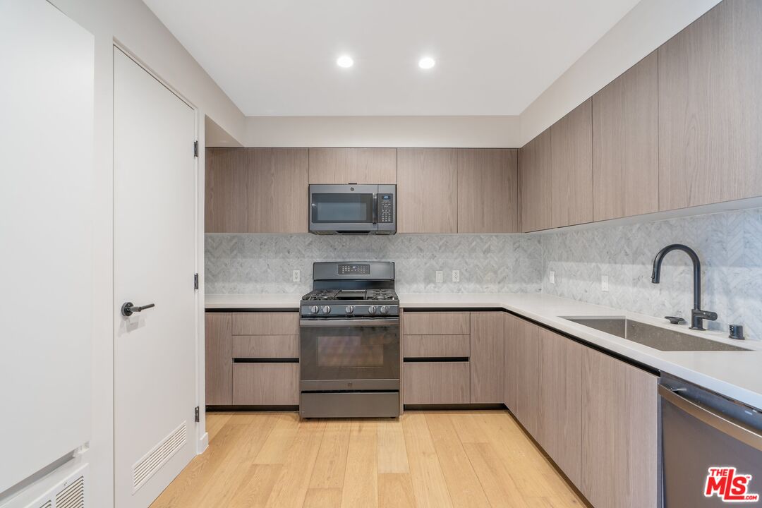 Kitchen with light wood cabinets, stainless-steel appliances, patterned backsplash, and a deep sink.