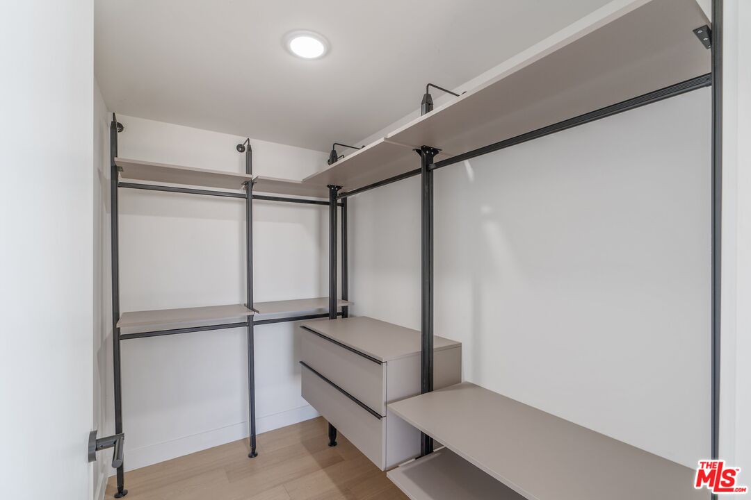 Walk-in closet with built-in shelves, hanging rails, drawers, and light wood flooring.