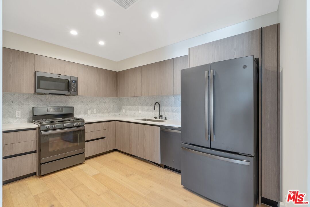 Kitchen with gray wood cabinets, patterned backsplash, gas range, and large French-door refrigerator.