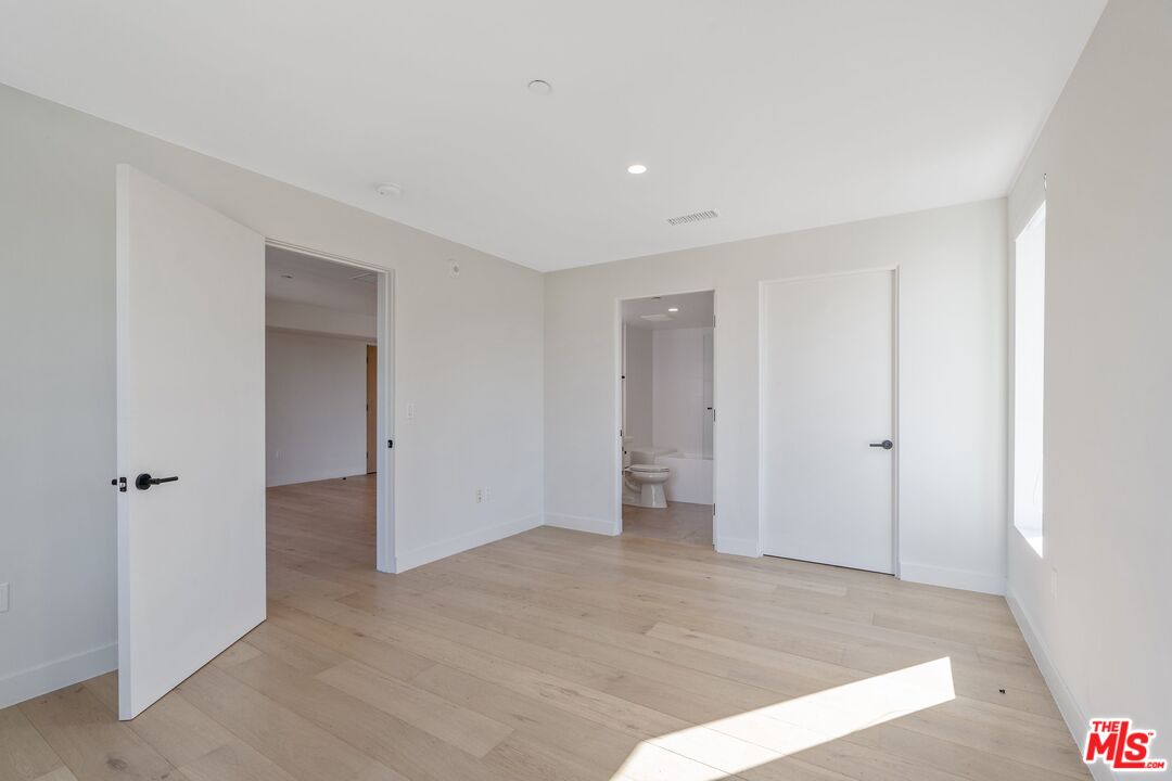 Empty bedroom with pale wood floors and a bathroom visible through the open doorway.
