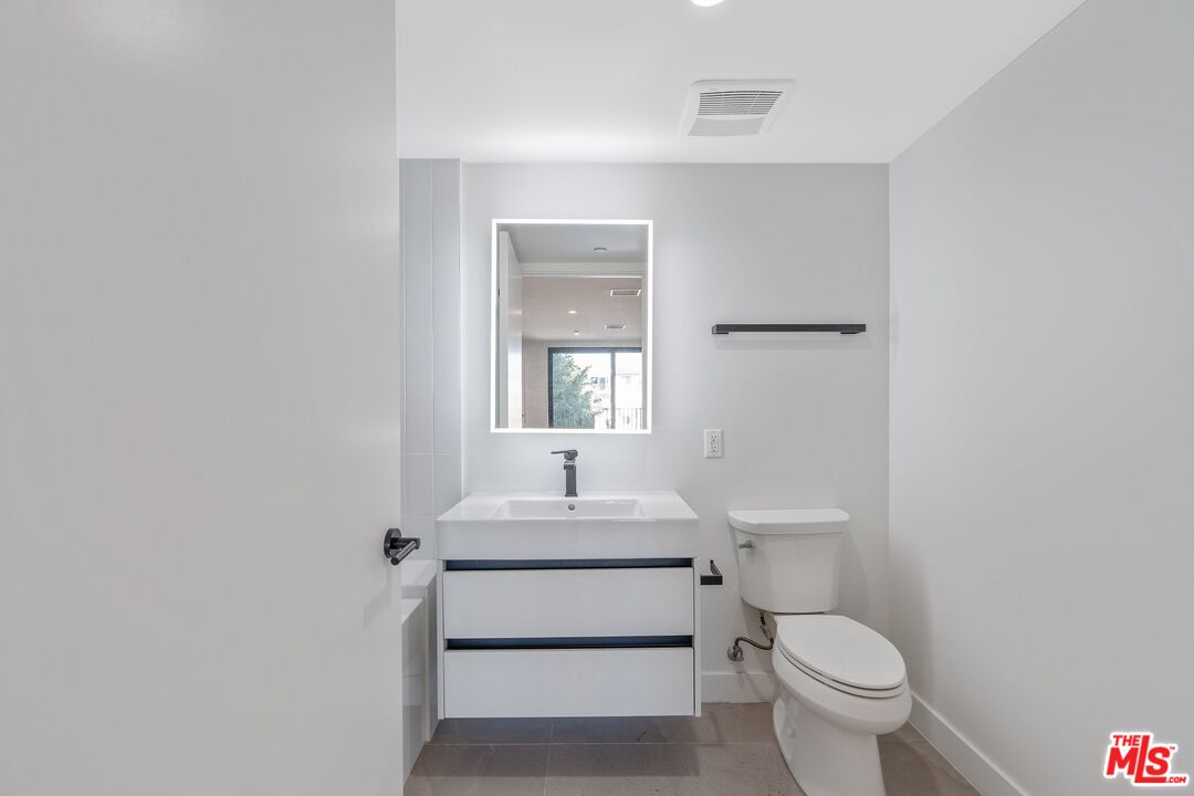 Bathroom with a floating white vanity, rectangular mirror, toilet, and gray tile floor.