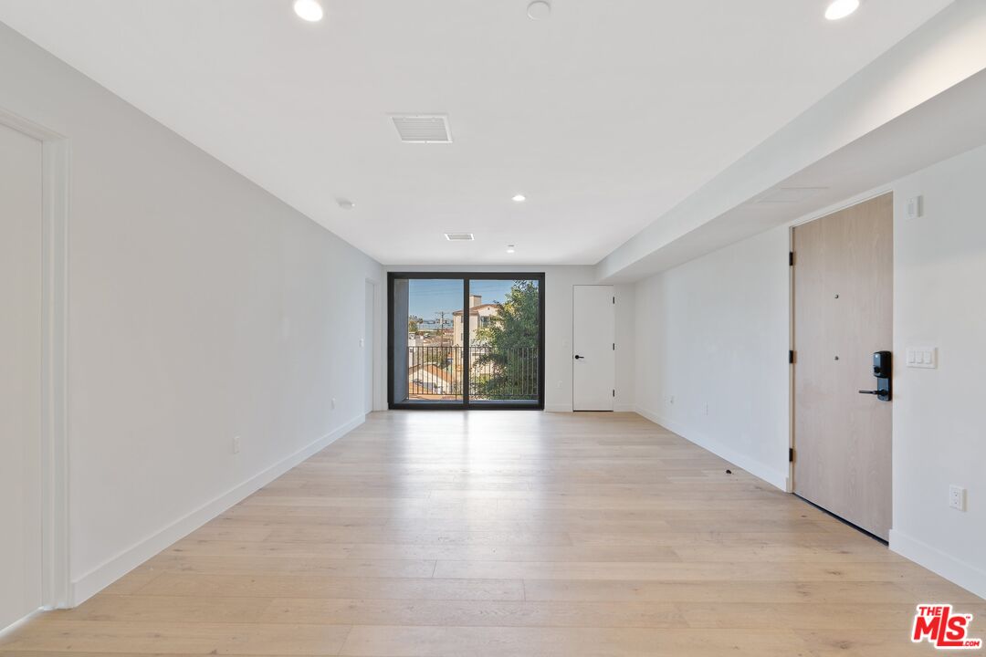 Vacant living area with pale wood floors and sliding glass doors opening to a balcony.