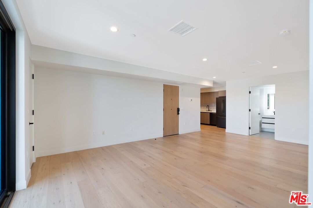 Vacant living area with pale wood floors, recessed lights, and an open kitchen.