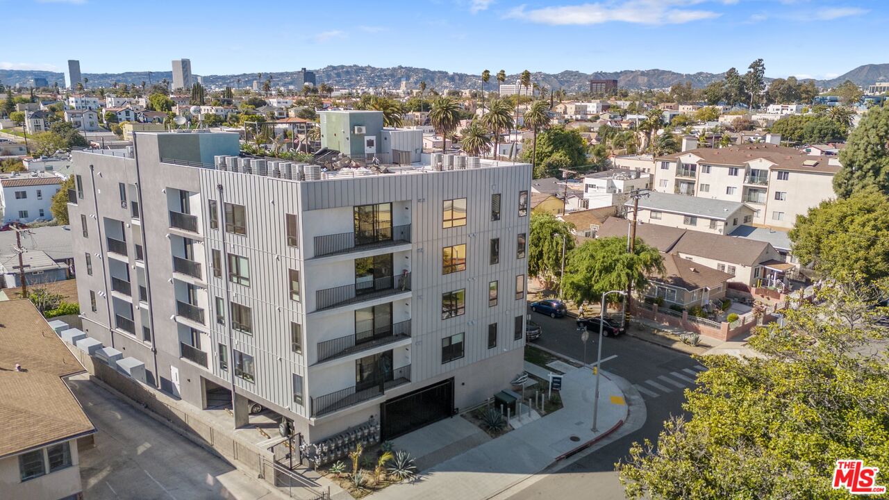 Modern gray apartment building with balconies, rooftop equipment, and surrounding Los Angeles neighborhood.
