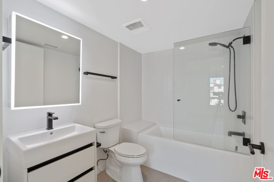 Modern bathroom with a glass-enclosed tub and shower, white vanity, and illuminated mirror.