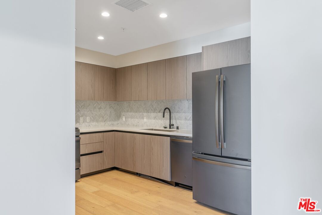 Modern kitchen with light wood cabinets, patterned tile backsplash, and a stainless steel refrigerator.