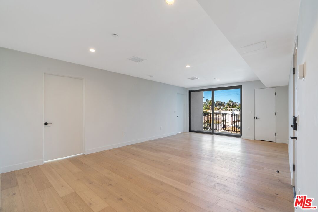 Empty condo living room with light wood floors and sliding glass doors to a balcony.